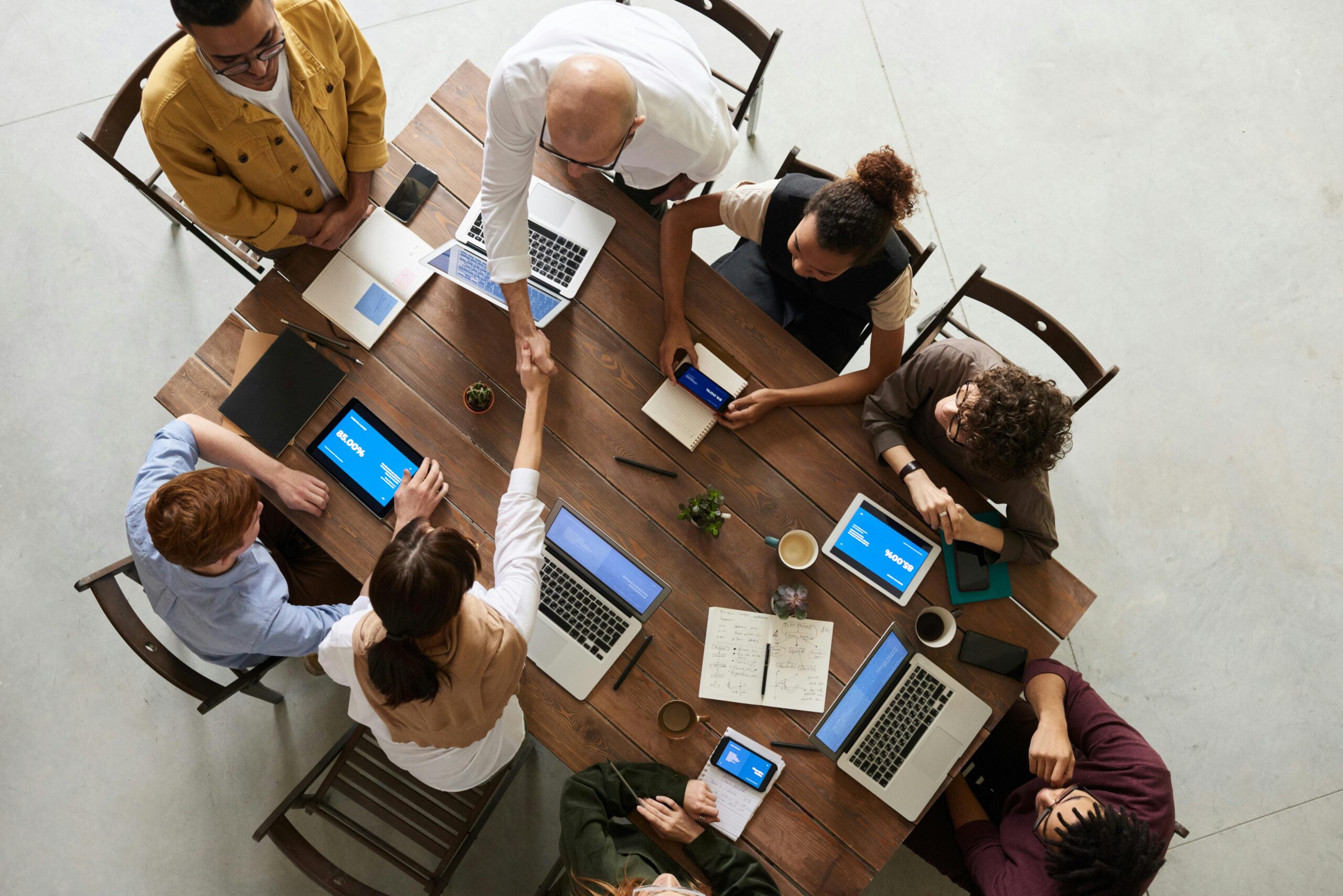 A birds-eye view of a group of people in a meeting with a woman and an older man shaking hands in agreement.