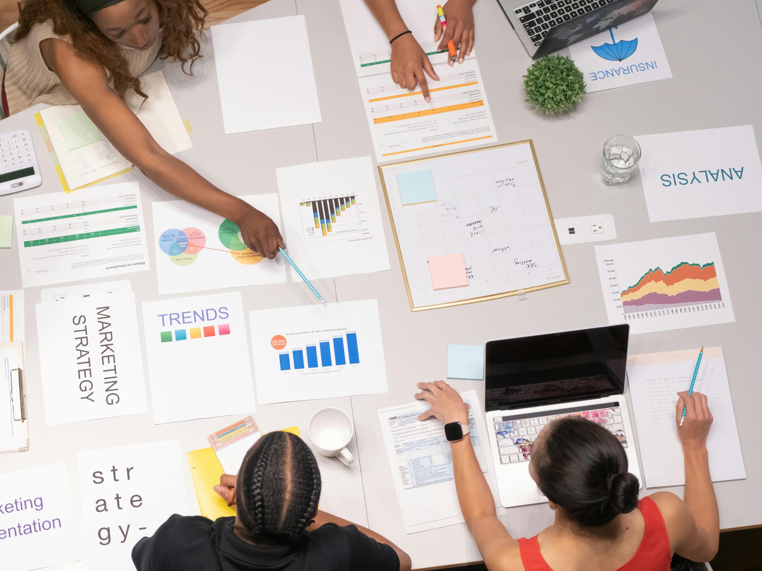 A bird's-eye view of a group of people discussing marketing trends and strategies with various different charts and graphs resembling data.